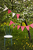 Blühender Kirschbaum mit Wimpelkett, darunter filigraner Stuhl