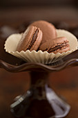 Three chocolate macarons in paper cups on a cake stand