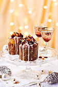 Mini fruit cakes topped with dried fruit and drizzled with icing, served on a cake stand alongside Christmas cocktails