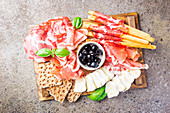 Cold meat plate with cheese, olives and bread on cutting board over gray stone background