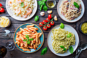 Several plates of pasta with different kinds of sauce over wooden background (Italian food)