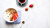 Müsli mit Joghurt und Erdbeeren und eine Tasse Kaffee auf Marmortisch