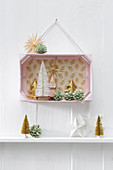 3D diorama of Christmas decorations in pink-painted fruit crate hung on wall