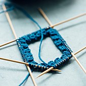 A blue sock being knitted on double pointed needles
