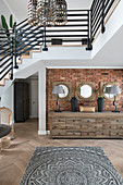 Chest of drawers against brick wall below staircase in open-plan interior