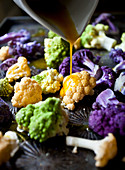 White cauliflower, purple cauliflower and romanesco broccoli florets being drizzled with turmeric oil