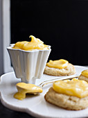 A white dish with lemon curd, alongside mini shortcakes topped with lemon curd