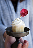 A woman holding a small vanilla cupcake with a pink cupcake topper