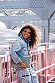 A dark-haired woman wearing jeans and a denim jacket standing on a bridge