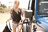 A young woman wearing a checked shirt and shorts standing by a jeep