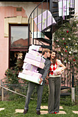 A couple with a stack of gift boxes standing at the bottom of a vintage spiral staricase