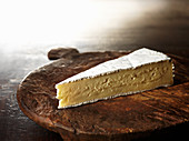 A slice of brie on an old wooden chopping board