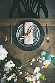 Gedeck mit Serviette, Besteck, Gläsern und Mandelblütenzweigen auf Vintage-Holztisch (Aufsicht)