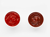 Zwei Schälchen Ketchup vor weißem Hintergrund (Aufsicht)