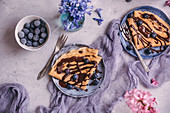 Crepes served on dessert plates drizzled with melted chocolate and topped with blueberries