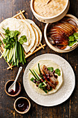 Peking Duck serving size with fresh cucumber, green onion, cilantro and roasted wheaten chinese pancakes with sauce Hoysin on wooden background