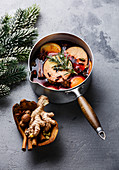Mulled wine hot drink with citrus, apple and spices in aluminum casserole and Fir branch on concrete background