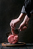 Man's hands cutting raw uncooked black angus beef tomahawk steak on bone