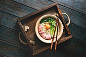 Udon noodles with egg yolk, sesame, mushrooms, boc choy, sliced sous vide cooked meat served in ceramic bowl
