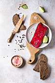 Piece of beetroot marinated salted salmon with sliced rye bread, pink salt, pepper and lime served on wooden cutting board