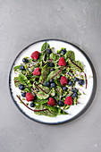 Green vegan salad with berries strawberry, blueberry, sprouts, young beetroot leaves on ceramic plate