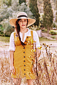 A brunette woman wearing a hat, a white shirt and a mustard-yellow dress