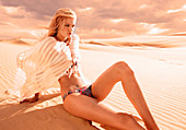 A blonde woman wearing a beach cape and a bikini in a desert