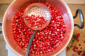 Lingon berry jam being made, raw lingon berries in a pot with draining spoon