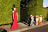 A woman wearing a long, red dress with a black headpiece and dressed-up children walking down the road