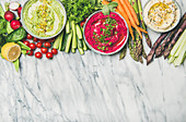 Chickpea, beetroot, spinach hummus dips with vegetables on marble background