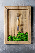 Raw uncooked organic green pea in wooden tray with fork over grey texture backgroundt