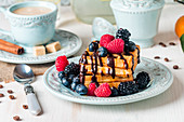 Fresh homemade brussels waffles with berries, chocolate and coffee for breakfast on white wooden background