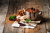 Mug of hot chocolate with cinnamon sticks over dark wooden background.