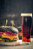 Gourmet black burger with berry sauce and beer on wooden table and dark background