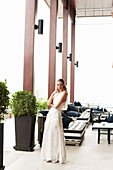 A blonde woman on a terrace wearing an elegant white dress