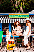 Zwei Frauen und ein Mädchen in hellen, sommerlichen Outfits vor Eisdiele