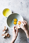 A womans hands separating eggs whites from egg yolks, with a mixing bowl