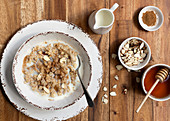 Traditional oatmeal porridge in a bowl with sliced almonds, cinnamon, honey and a jug of milk