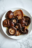 Soaked siitake mushrooms in white bowl on white marble table