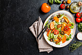 Fresh salad with persimmon, chicken and greens on black background, top view