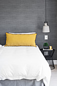 Yellow pillow on bed against grey wall