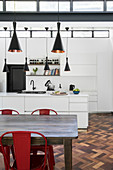 Wooden dining table with red chairs in front of white fitted kitchen