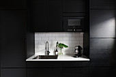 Modern, black fitted kitchen with white worksurface in niche