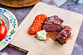 Raw beef loin steaks with tomatoes and herb butter on a wooden board