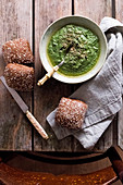 Spinach pesto in a bowl with bread at a wooden table and a chair