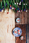 Blue plates with little cakes and raspberries on a wooden background with flowers above them