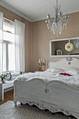 Weißes Holzbett und Kronleuchter in nostalgischem Schlafzimmer mit Tapete
