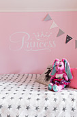 Soft toy on bed against pink wall in girl's bedroom
