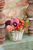 Buntes Gesteck mit Herbstblumen und Tomaten im Korb