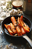 Baked carrots with thyme and sea salt on heavy frying pan on rustic background